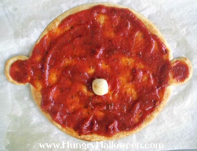 Top the vampire shaped pizza crust with pizza sauce. 