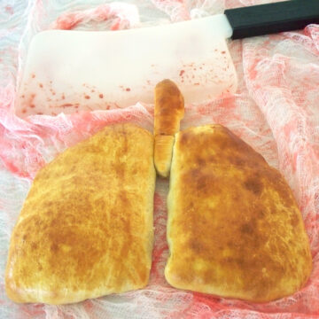 lung calzones on a piece of bloody gauze fabric next to a bloody meat clever.