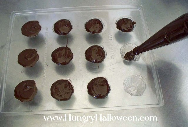 piping dark chocolate into a plastic pumpkin candy mold. 
