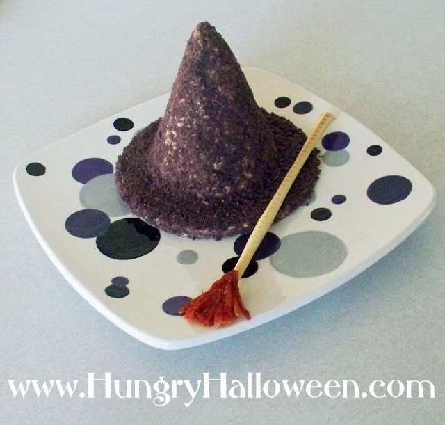 witch hat cheese ball on a polka dot plate with a breadstick broomstick. 
