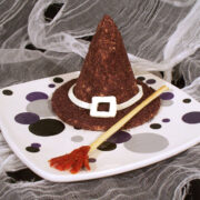 Halloween cheese ball witch hat and a breadstick broom served on a purple, black, and white polka dot platter.