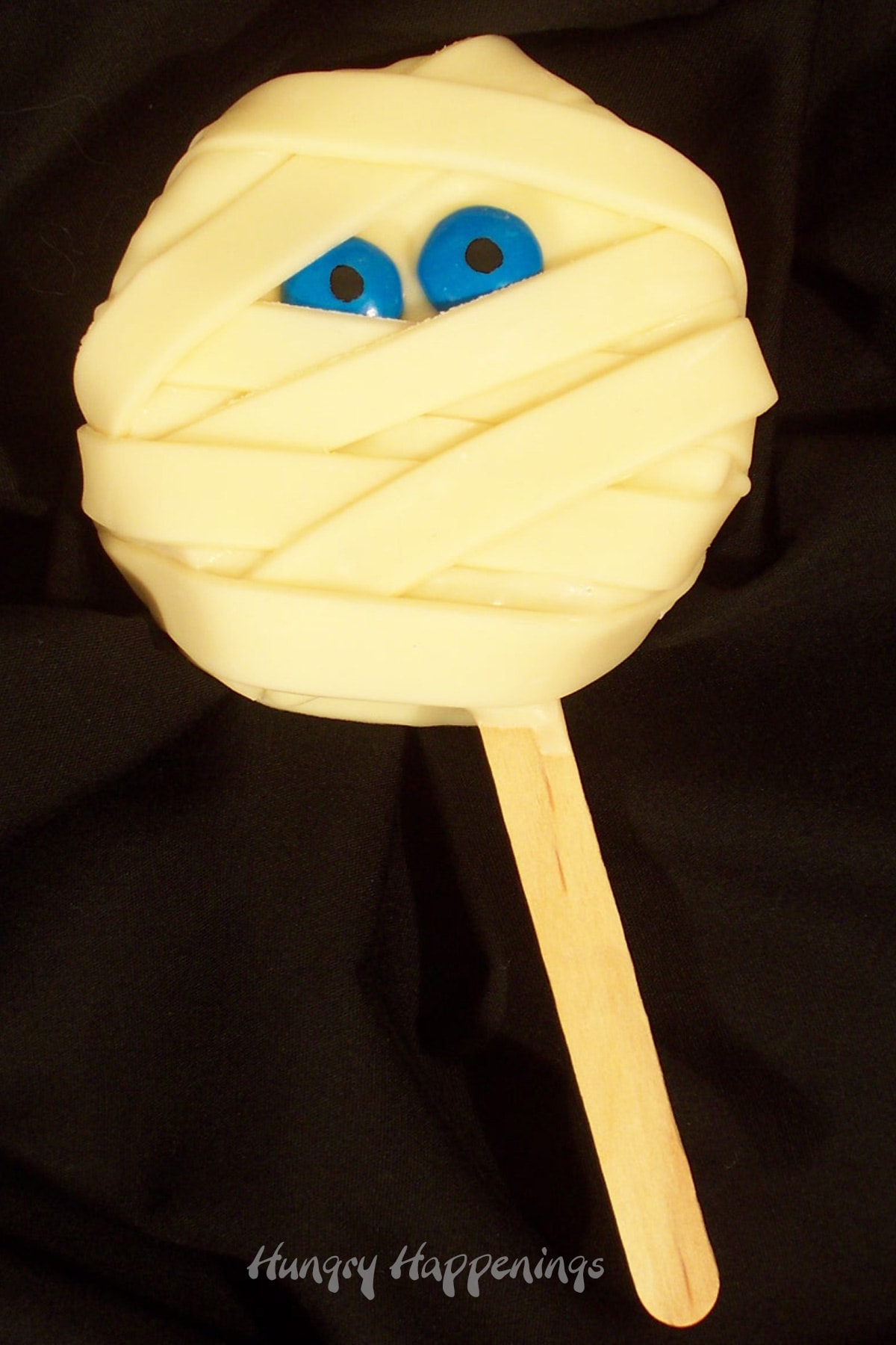 rice krispie treat mummy lollipops with blue M&M eyes on a black table. 