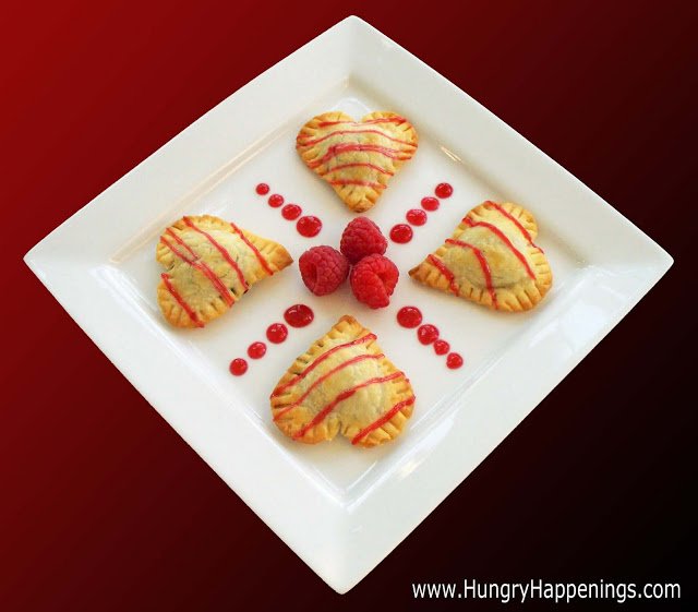 heart-shaped chocolate hand pies filled with chocolate hearts and topped with raspberry sauce served with raspberries.