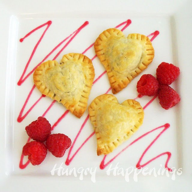 mini heart-shaped chocolate pies on a white plate with a drizzle of raspberry sauce and fresh raspberries