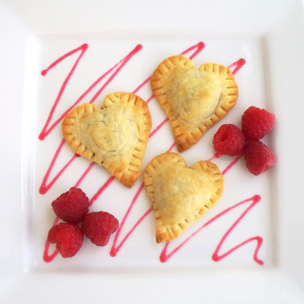 Chocolate Pastry Hearts served with a drizzle of raspberry sauce and fresh raspberries.