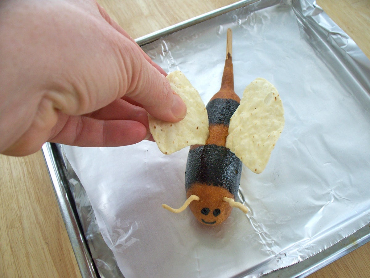 inserting tortilla chip wings into a corn dog bumble bee.