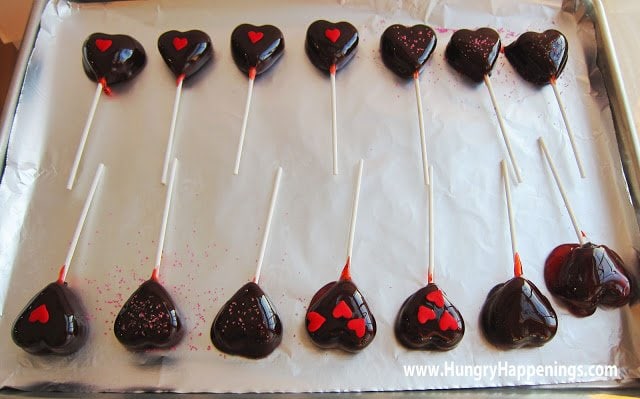 Homemade cherry Tootsie Pop Hearts cooling on a lined baking tray.