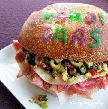 Muffaletta sandwich filled with lunch meat, olives, pimentos, and more decorated for Mardi Gras.