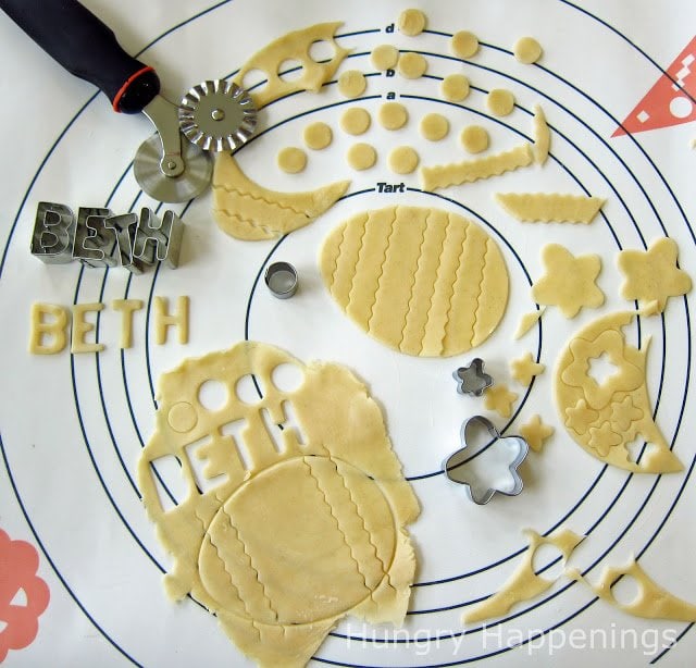cutting out pie dough decorations including the name Beth, flowers, stripes, and polka dots using cookie cutters and a pastry wheel.