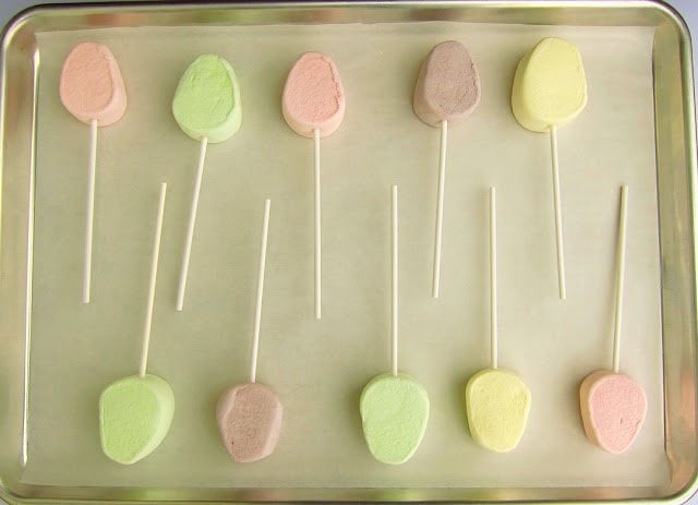 Jet-Puffed Marshmallow Eggs with sticks on a parchment paper-lined baking pan. 