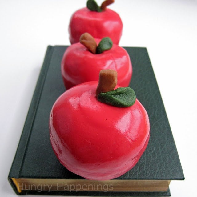 chocolate caramel fudge shaped apples dipped in red candy melts with a chocolate stem and green candy leaf. 