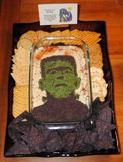 spinach artichoke dip decorated with Frankenstein surrounded by crackers and blue corn tortilla chips. 