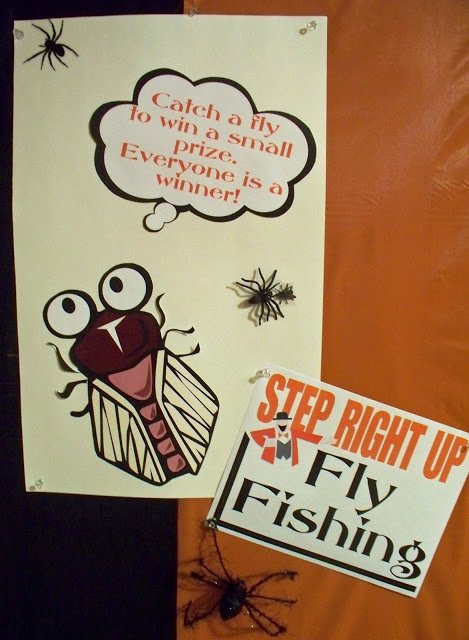 Fly Fishing carnival game signs on orange and black striped wall.