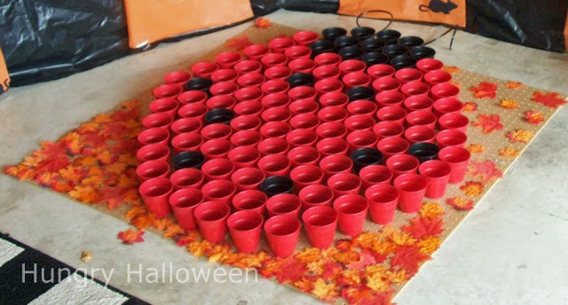 red and black plastic cups arranged to look like a ladybug set on a peg board covered in fabric fall leaves. 
