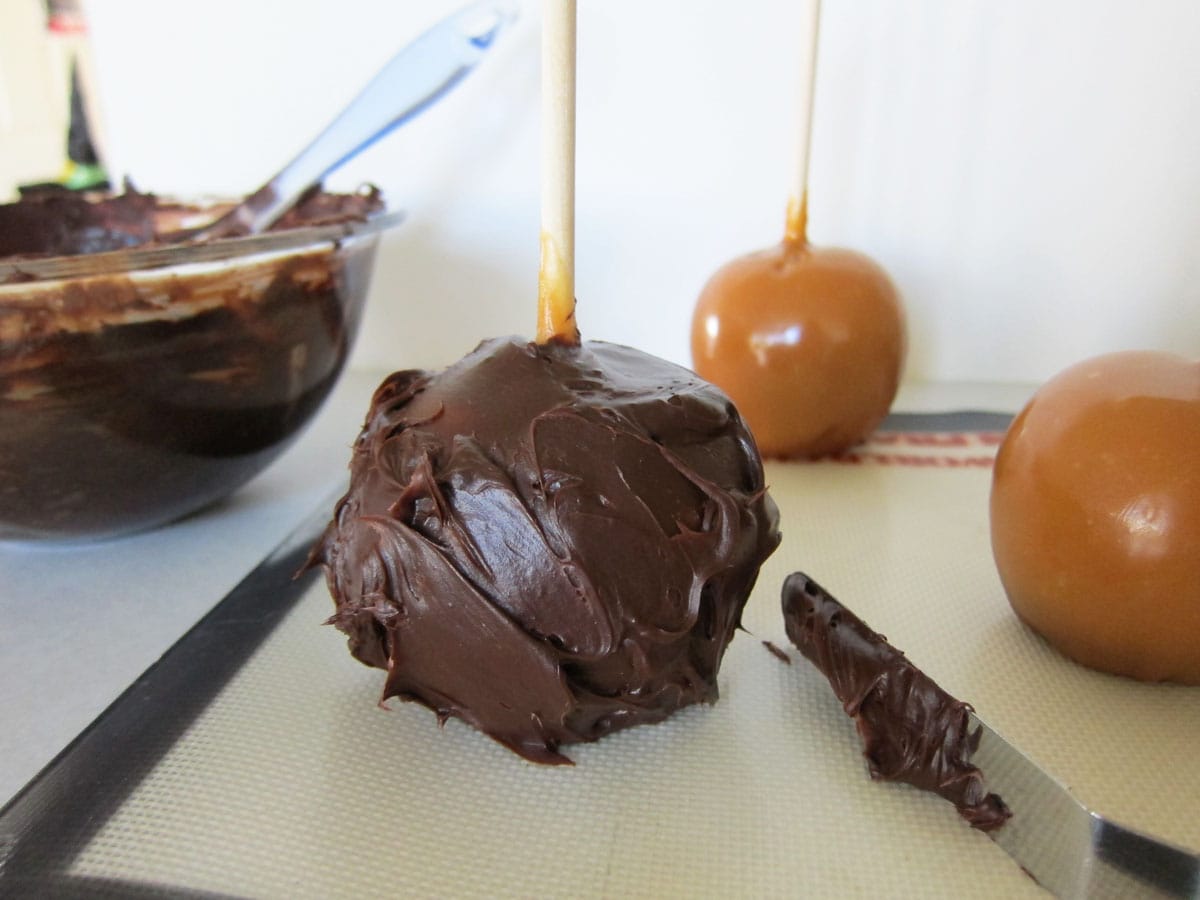 frosting a caramel apple with chocolate ganache.