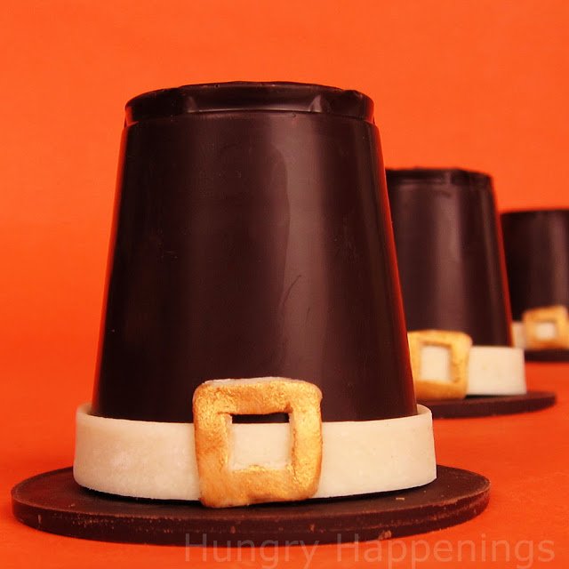 three chocolate pilgrim hats displayed on an orange background. 