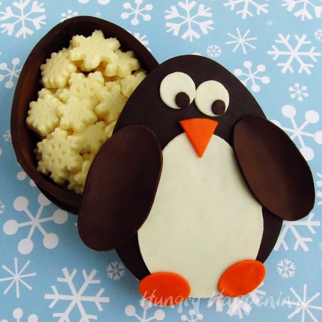 dark chocolate box shaped and decorated like a penguin filled with white chocolate snowflakes. 
