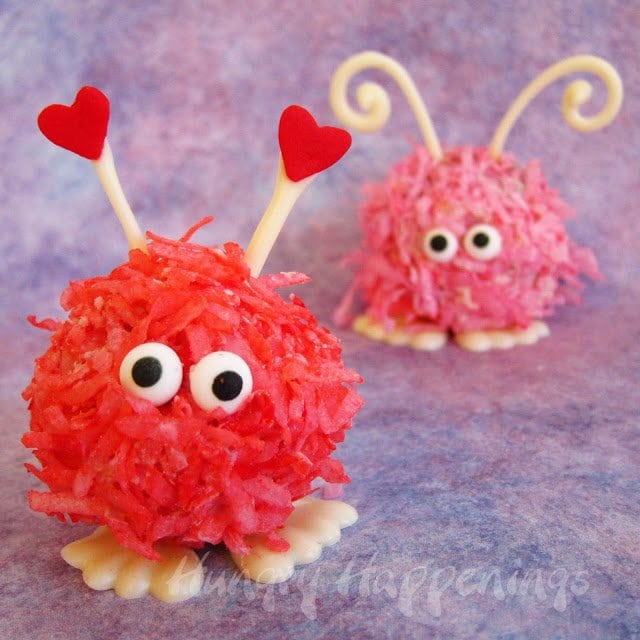red and pink warm fuzzy cake balls coated in colored coconut with candy eyes and white chocolate feet and antennae.
