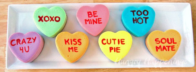 purple, green, orange, pink, yellow, and blue conversation heart cheesecakes on a long white plate