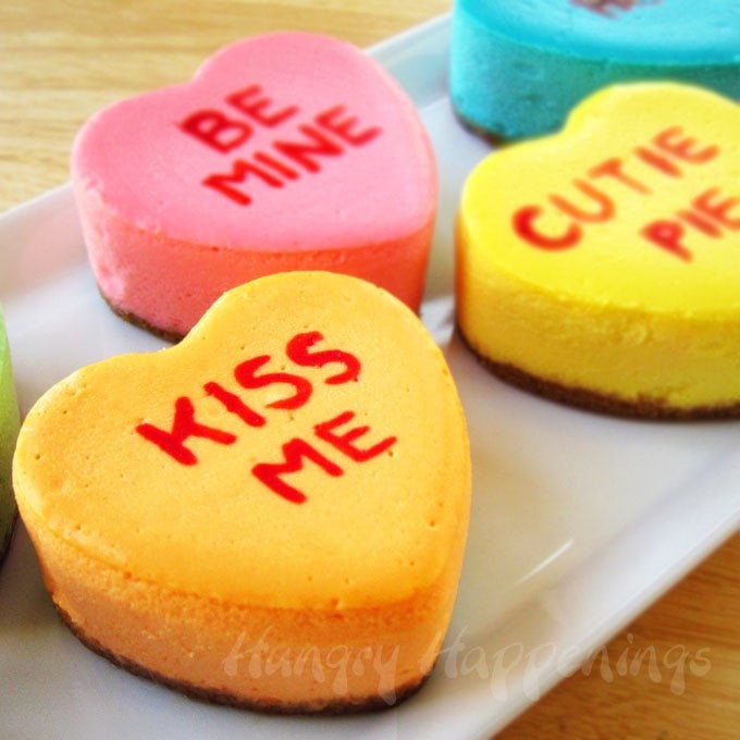 orange, pink, yellow, and blue heart-shaped conversation heart cheesecakes personalized with Valentine's Day messages