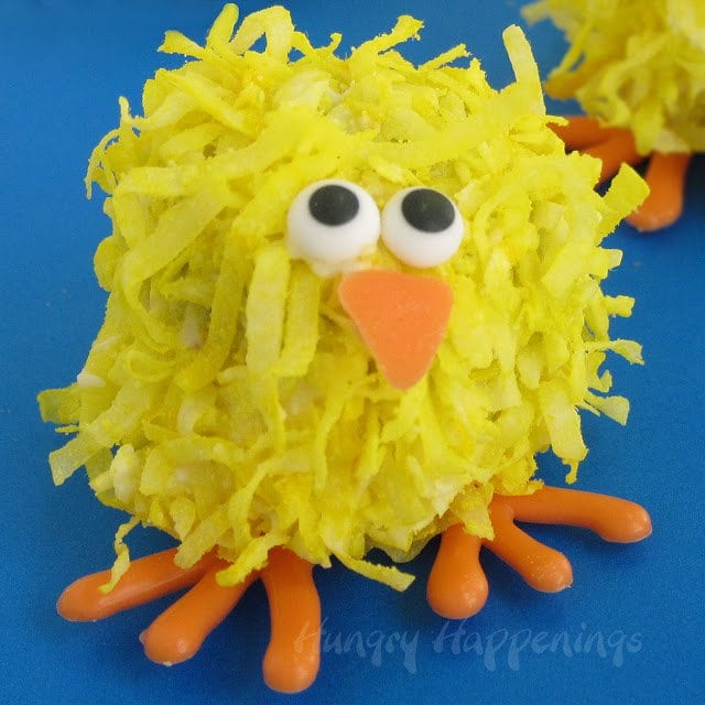 a single baby chick cake ball with orange candy feet and beak, candy eyes, and yellow coconut feathers.