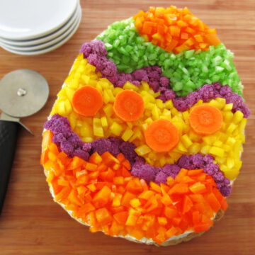 veggie pizza Easter egg topped with orange and yellow peppers, purple cauliflower, carrots, and celery.