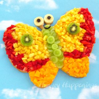 Butterfly fruit pizza topped with pineapple, grapes, strawberries,peaches, banana, and kiwi and decorated with chocolate chip eyes.
