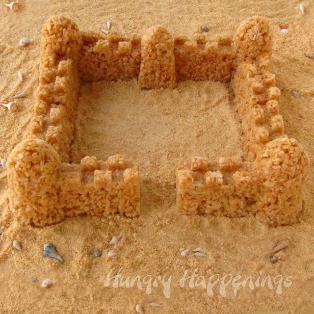 Caramel Rice Krispie Treat Sandcastle surrounded by cookie crumbs and seashells.
