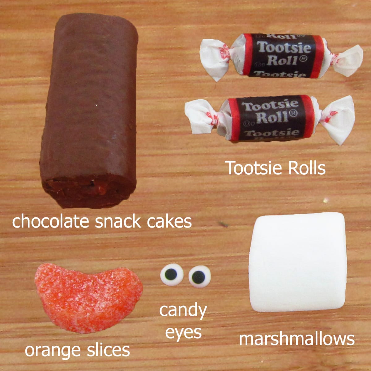snack cake penguin ingredients including chocolate cake rolls, Tootsie Rolls, orange slices, candy eyes, and marshmallows. 