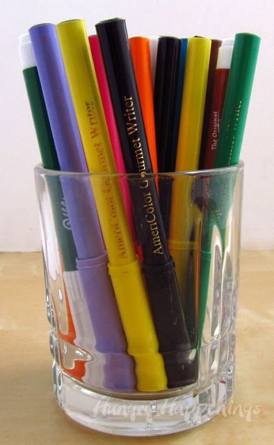 a clear glass filled with various food coloring markers and edible ink pens. 