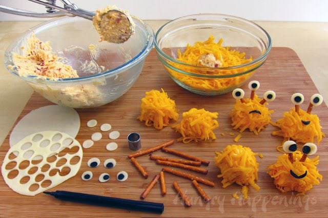 making mini cheese ball monsters coated in shredded cheddar cheese with pretzel stick an cheese eyes. 