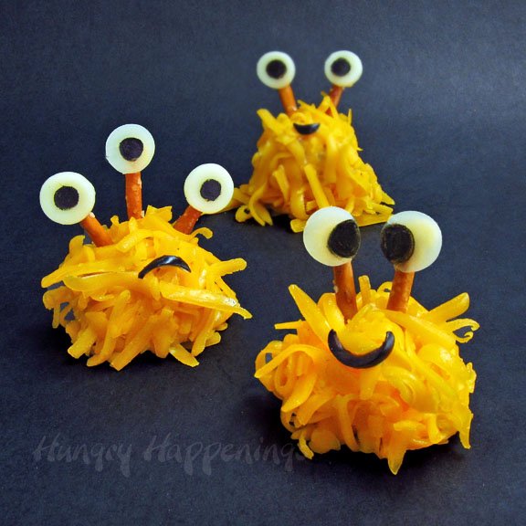 orange cheddar cheese-coated cheese ball monsters with pretzel and cheese eyes. 