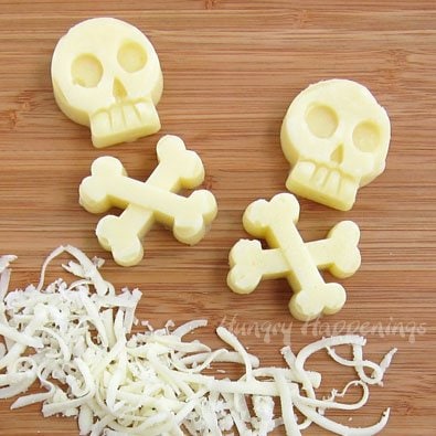 Mozzarella cheese skulls and crossbones set on a cutting board with freshly shredded Mozzarella cheese. 