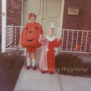 one young girl in a pumpkin costume next to a younger girl in a clown costume in front of a house in the 1970s.