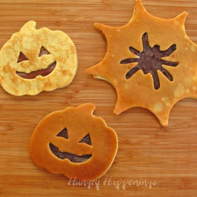 Pumpkin pancakes with Jack-O-Lantern faces and spider web pancakes with spiders cut out are filled with chocolate hazelnut spread or caramel spread. 