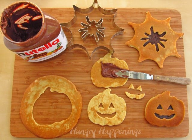 Cut pancakes using spider web or pumpkin cookie cutters then cut out spiders or Jack-O-Lantern faces and fill the pancakes with Nutella or dulce de leche.