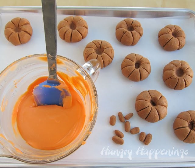 caramel pumpkins, caramel fudge stems, and a bowl of melted orange candy melts on a parchment paper-lined baking sheet. 