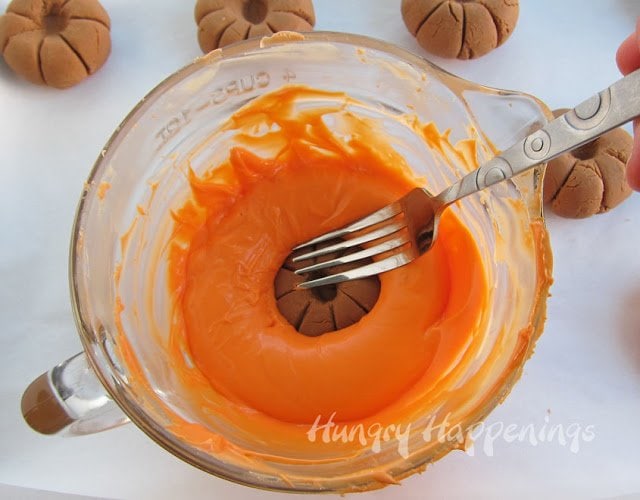 submerging fudge pumpkin into orange candy melts using a fork. 