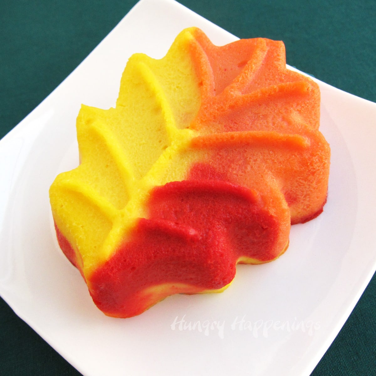 single red, yellow, and orange fall leaf-shaped cheesecake on a small white plate. 