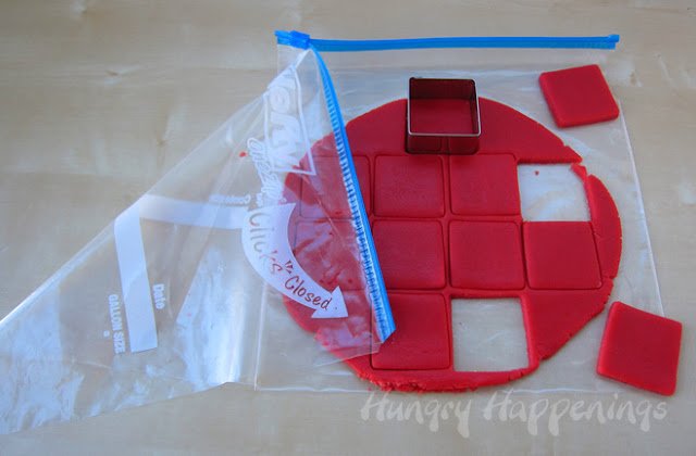cutting red cookie dough using a square cookie cutter. 