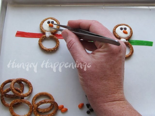 adding two mini chocolate chip eyes and an orange candy-coated sunflower nose to the white chocolate snowman pretzel. 