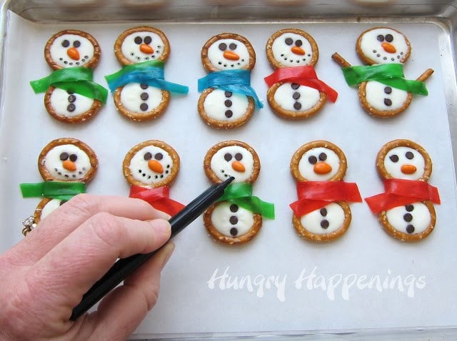 drawing smiled onto a tray of pretzel snowmen using a black food coloring marker. 