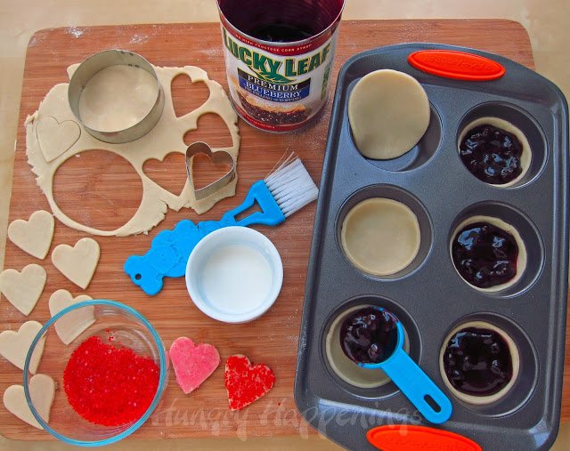 filling mini pie crusts with blueberry pie filling and topping heart-shaped pie dough with red and pink sugar.
