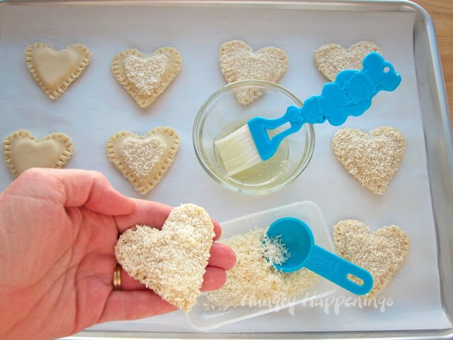 brush heart-shaped pastries with egg white and sprinkle with parmesan cheese