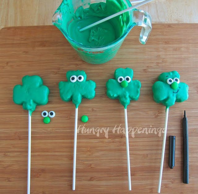 adding candy eyes, green M&M noses, and smiles using a black food coloring marker to the shamrock treats