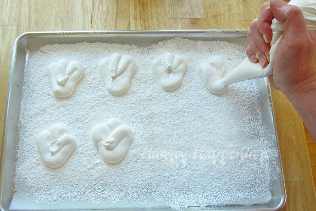 piping bunny feet onto a cookie sheet topped with powdered sugar. 