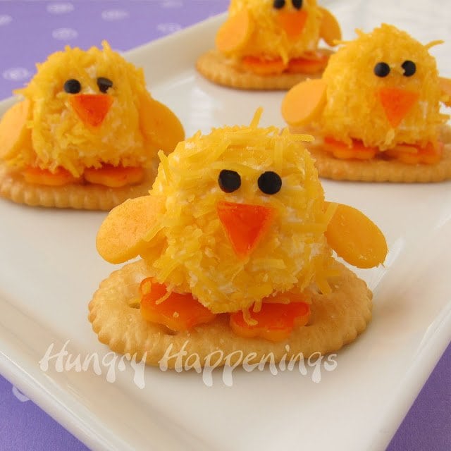 four bite-sized cheese ball chicks served on a white plate on a purple tabletop. 
