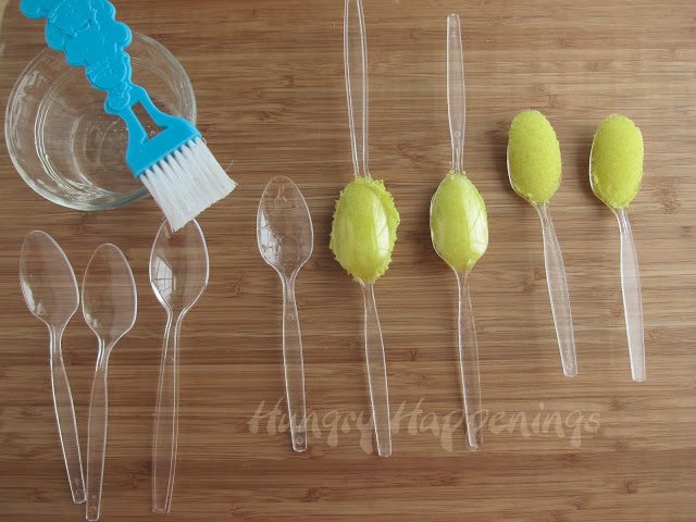brushing plastic spoons with corn syrup and pressing the yellow sugar mixture between two spoons. 