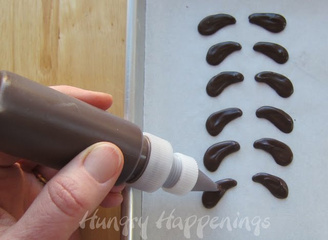 piping chocolate ears onto parchment paper.