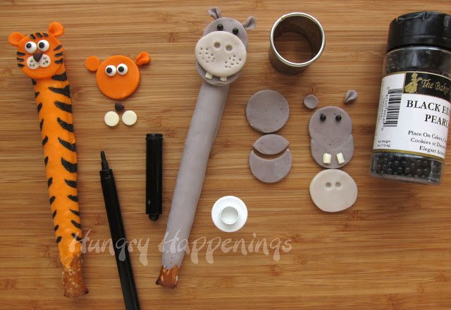 decorating a pretzel tiger using white, orange, and brown modeling chocolate with black food coloring stripes, and a hippo pretzel using light and dark grey modeling chocolate and black sugar pearls. 